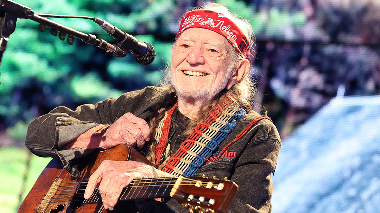 Willie Nelson smiling holding a guitar onstage