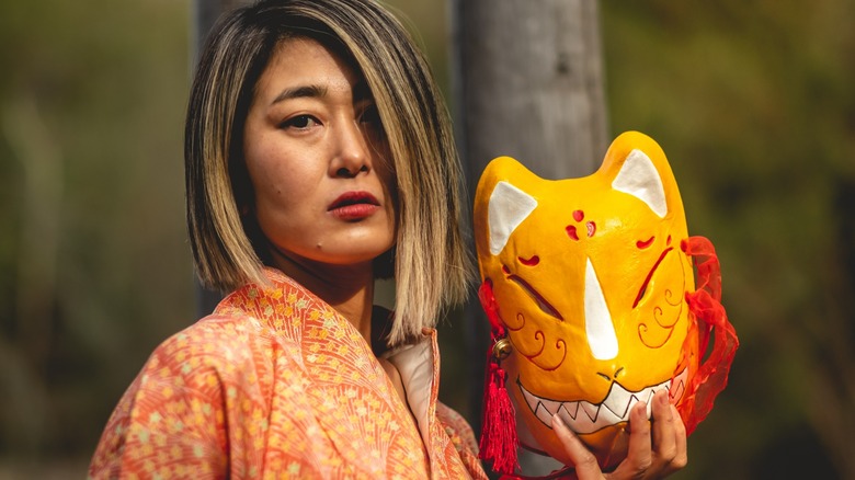 Asian woman holding a kitsune mask