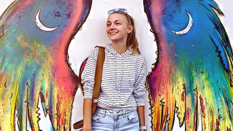Gabby Petito smiling in front of a rainbow angel wing mural
