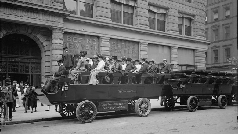 The "Seeing New York" electric omnibus waits in front of the Flatiron Building, filled with well-dressed tourists