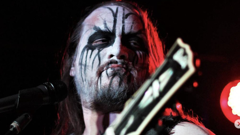 Member of Wormreich on stage playing guitar in face paint looking to the side all scary