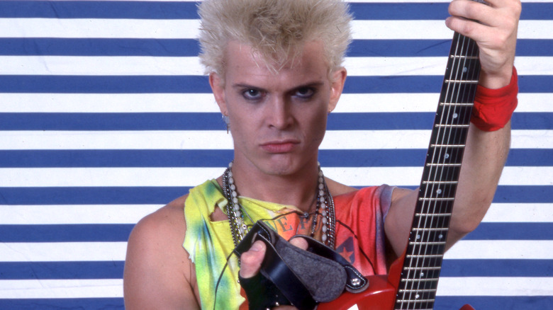 Billy Idol fiercely holding red guitar blue striped background