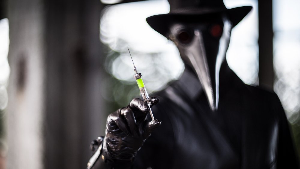 Plague doctor shows a syringe with a poisonous green liquid. 