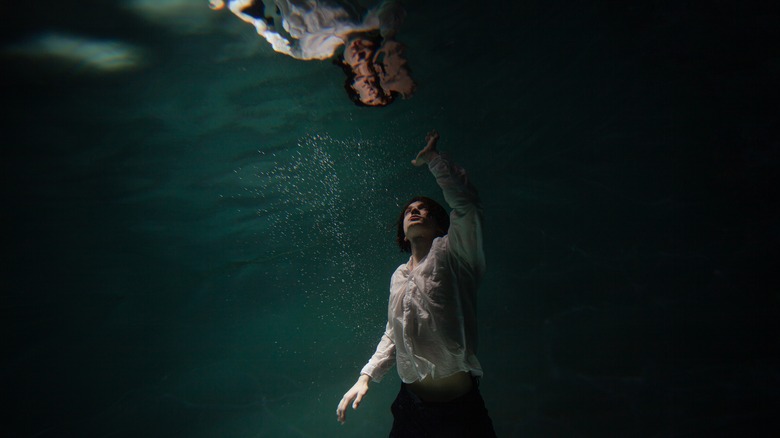 Person underwater reaching up at their reflection