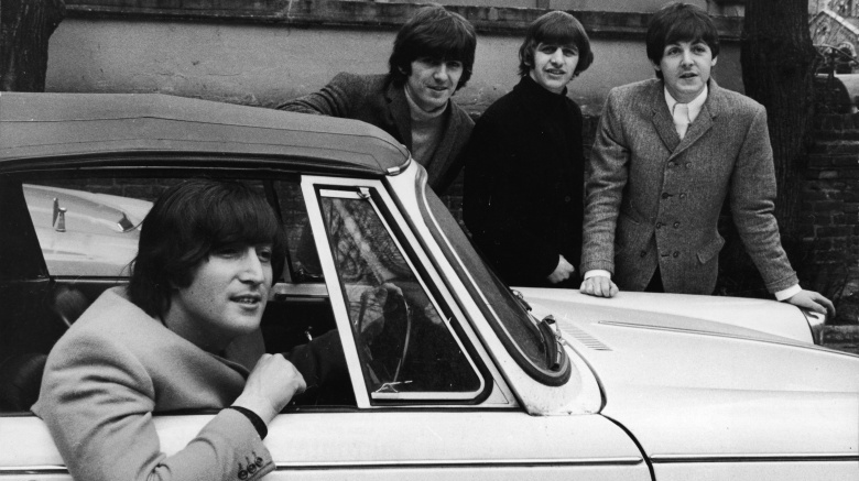 The Beatles posing near a car