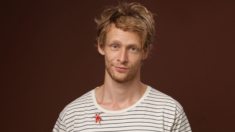 Johnny Lewis smiling striped shirt brown background