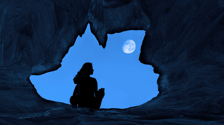 Woman in mouth of cave with moon