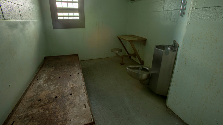 solitary confinement cell with cot, desk, and toilet