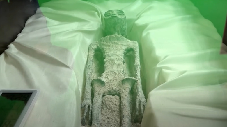 Green-lit alien corpse in white bedding