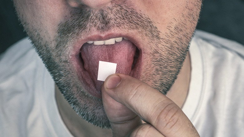 A man putting a hit of blotter acid on his tongue