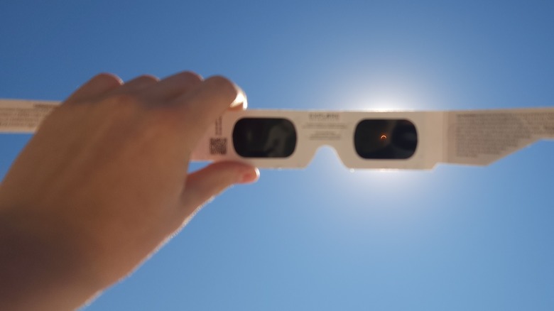 Hand holding eclipse glasses up to an eclipse