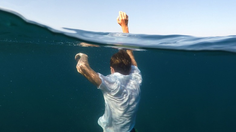 A young man submerged in water with raised hand
