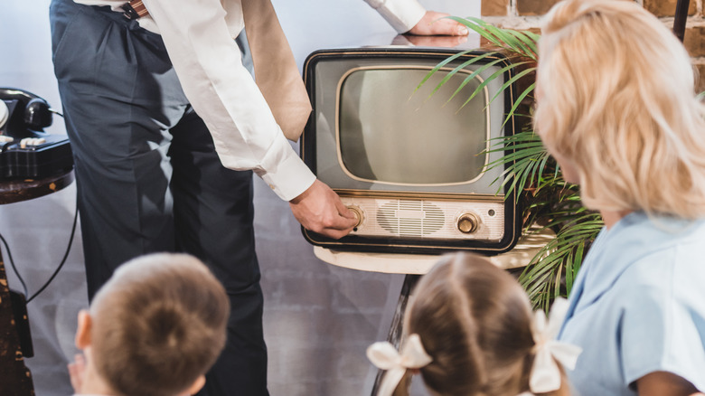 man turns on a 1950s television woman kids watching