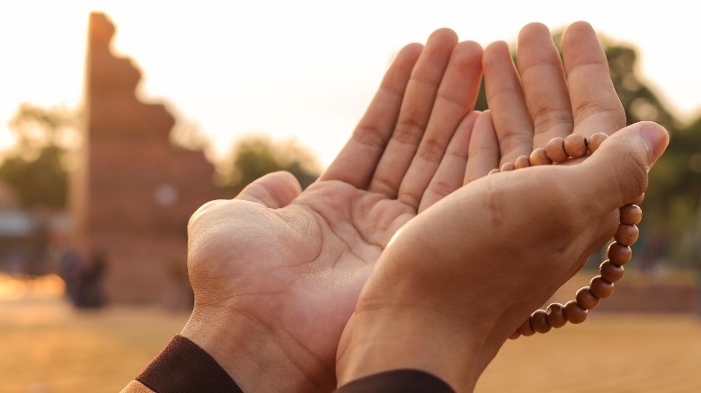 Close-up of hands holding Islamic beads at sunset