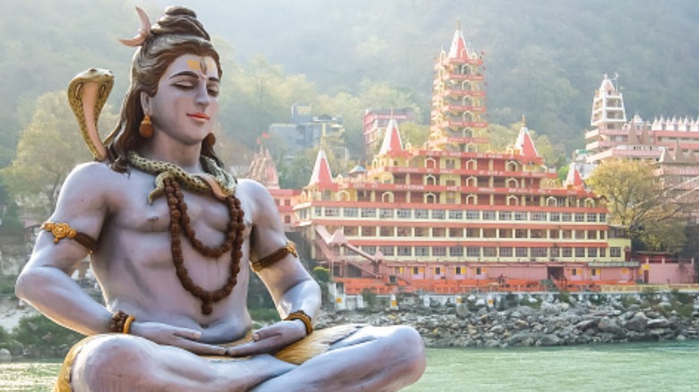 Statue of meditating Shiva by Ganges river and indian temple