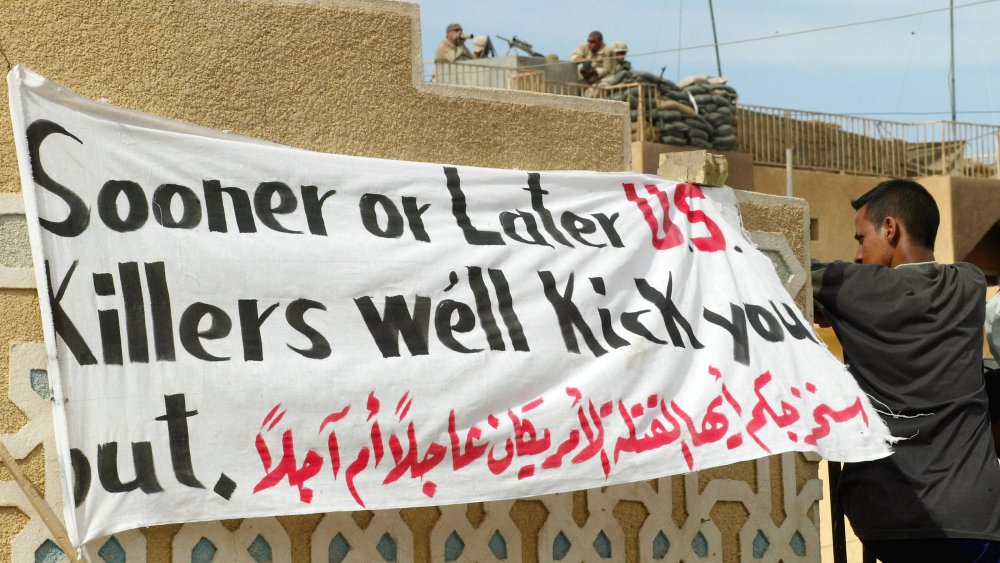 An Iraqi man in Fallujah in May, 2004, standing near a sign saying "Sooner or later US killers we'll kick you out."