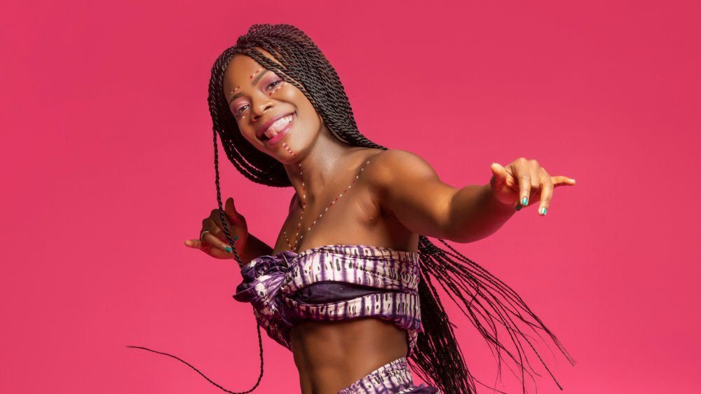 Grinning Black woman performing dance against a pink backdrop