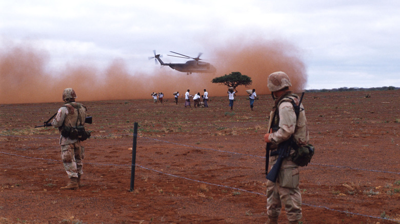 soldiers in a sandy field with helicopters