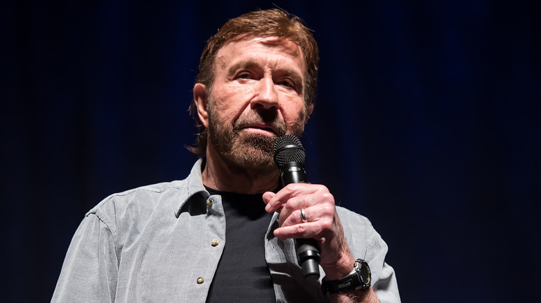 Chuck Norris holding a microphone against a black background