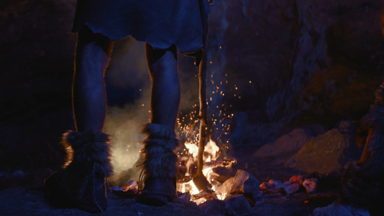 A lone prehistoric man standing in front of a fire