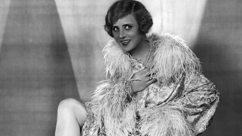 Ossi Oswalda posing in a feathered robe with a big smile