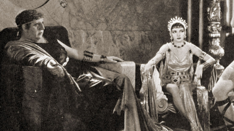 Charles Laughton as Emperor Nero sits in a throne in a toga with a woman to his left