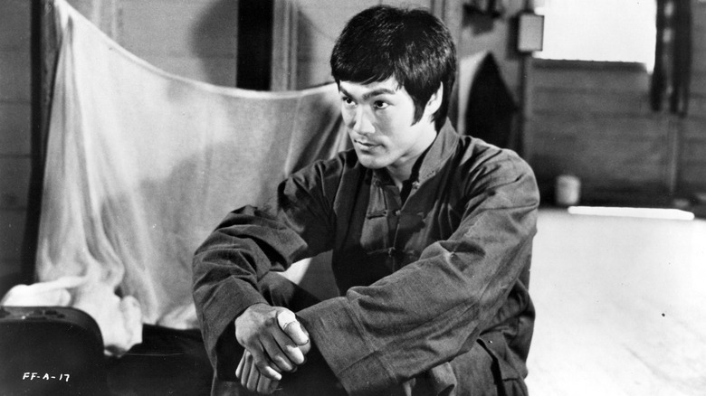 Bruce Lee sat hands folded chinese dress by blanket