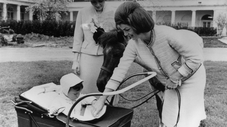 Jackie Kennedy pushing her son in a carriage on White House grounds