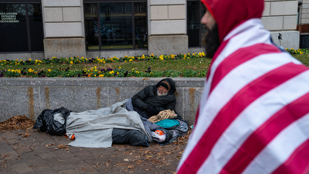 Man wearing US flag walks by homeless man
