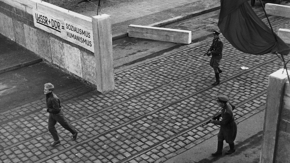 An East German man flees Berlin Wall border guards