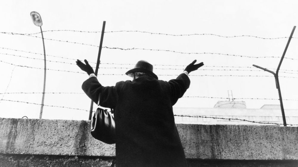 A woman waves over the Berlin Wall