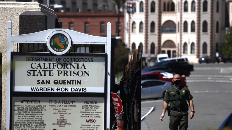 Security guard in mask near sign, San Quentin State Prison, California