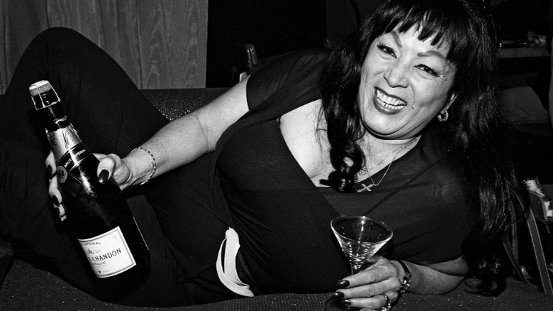 Black and white photo of Tura Satana smiling and holding a bottle of champagne and a glass
