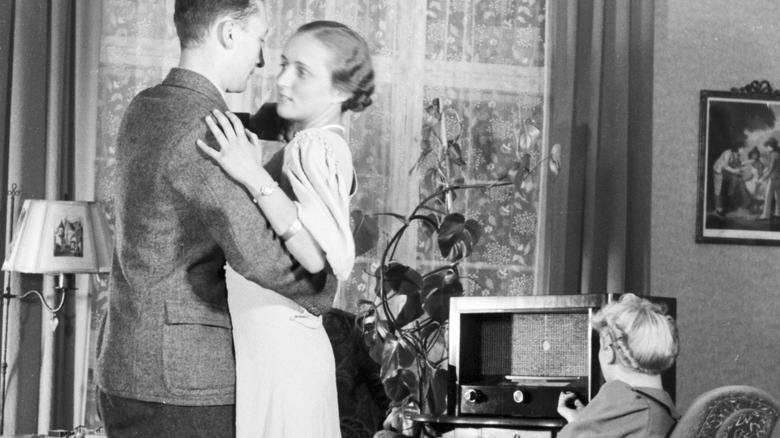 Couple dancing at home while woman turns knob on radio