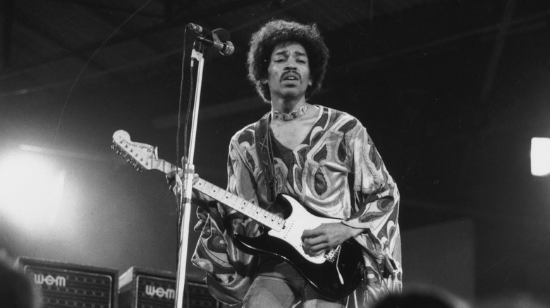 Jimi Hendrix performing on stage guitar patterned shirt