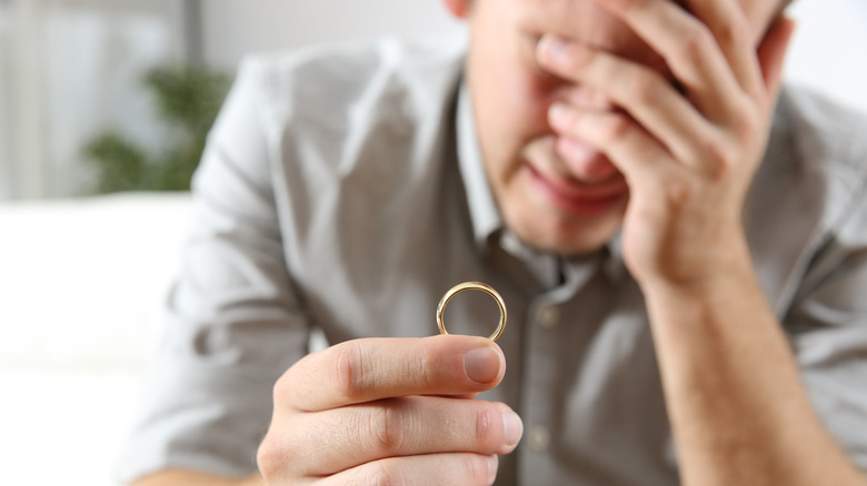 sad husband lamenting after divorce holding the wedding ring in a house