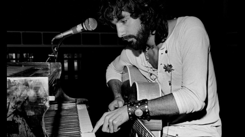 Cat Stevens holding a guitar and playing the piano