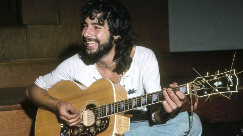 Cat Stevens smiling and playing the acoustic guitar in 1975