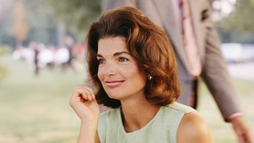 Jacqueline Kennedy Onassis sitting at a picnic table outside in a green dress 