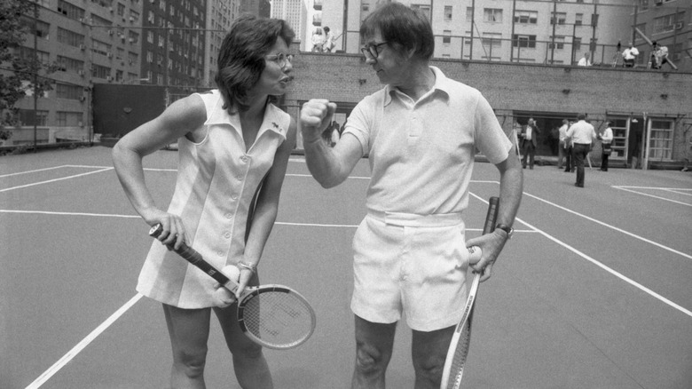 Billie Jean King and Bobby Riggs comically posing together on tennis court