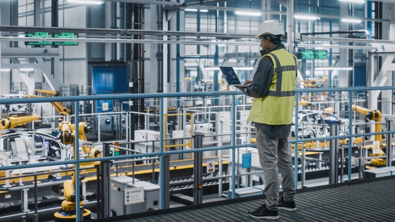 Person in high visibility vest on factory floor watching machines