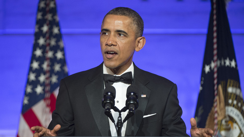 Obama gesturing talking event flags blue background