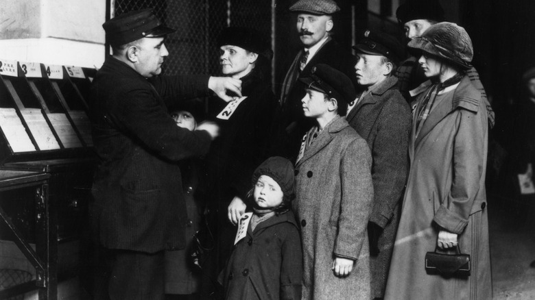 a customs official attaches labels to the coats of a German immigrant family on Ellis Island