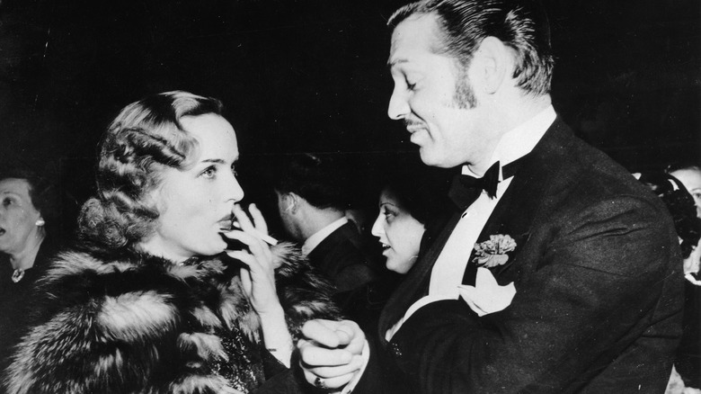 Carole Lombard smoking while Clark Gable looks down