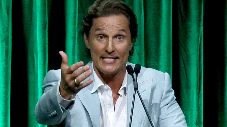 Matthew McConaughey raised hand speaking green curtain