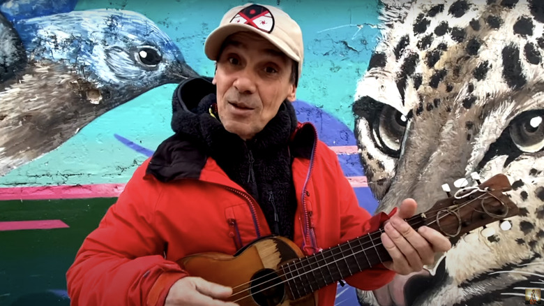 Manu Chao playing an ukulele in front of a street mural