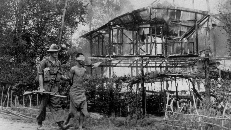 A British soldier escorts a Japanese prisoner as Burma burns around them