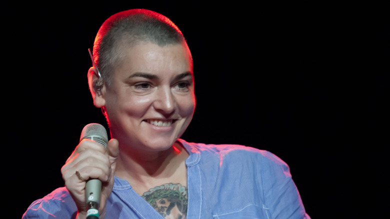Sinéad O'Connor smiling on stage with mic in blue shirt