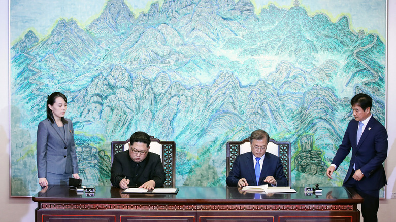 Kim Yo-jong stands next to table while Kim Jong-un and Moon Jae-in sign papers