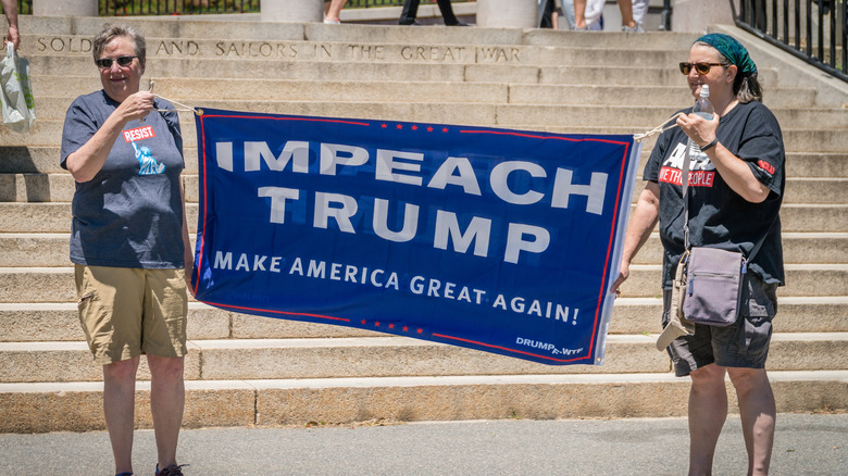 Two women hold an 'Impeach Trump' banner.